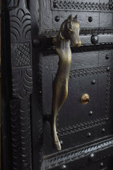 Decorative metal door handle shaped like a horse head on an ornate black door.
