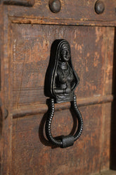 Decorative iron door knocker shaped like a woman on an old wooden door.