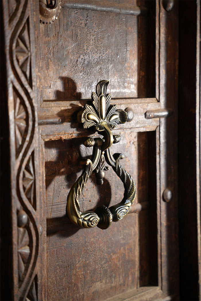 Decorative iron peacock door knocker on an ornate wooden door
