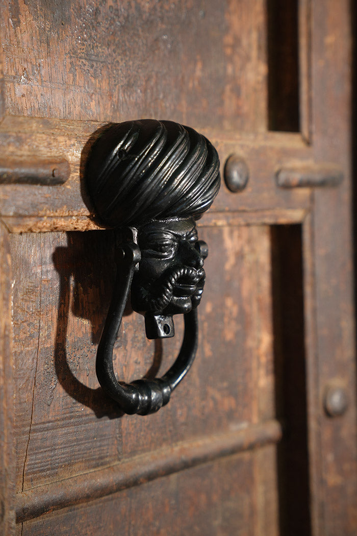 Iron door knocker with a face of Rajasthani man on a wooden door